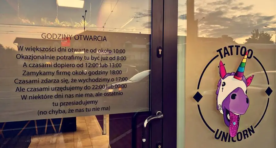 Wejście do studia Tattoo Unicorn z logo i godzinami otwarcia na szybie